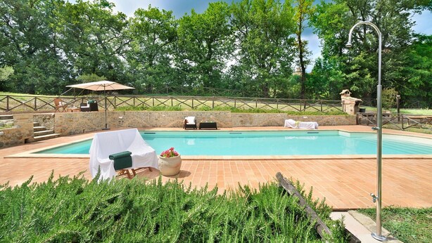 Ein Pool mit Steinmauer, Sitzgelegenheiten im Freien und üppiger Bepflanzung.