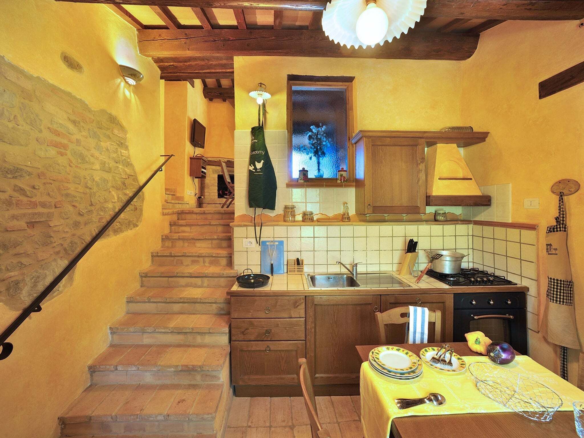 A compact kitchen with a wooden staircase, a dining area with a table set for two, and a small window with a view.