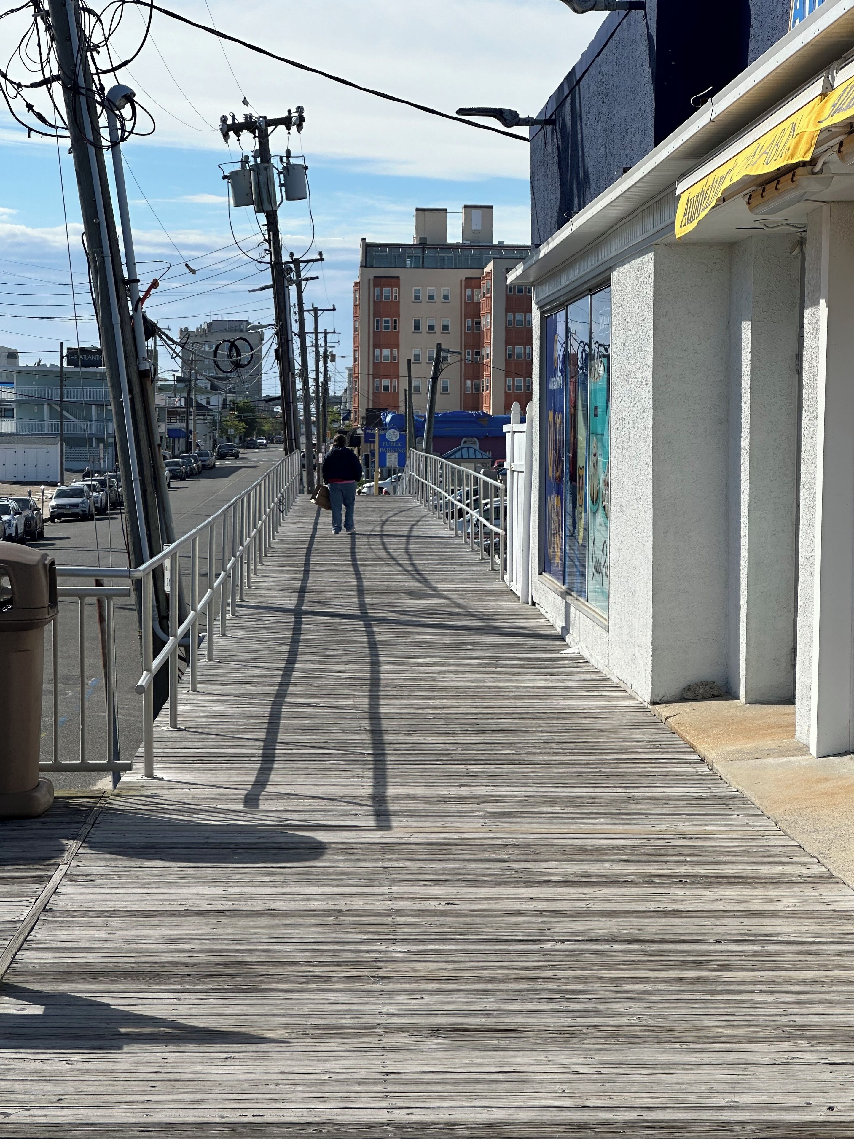 Un muelle de madera con un sendero peatonal, postes de servicios públicos y edificios al fondo.