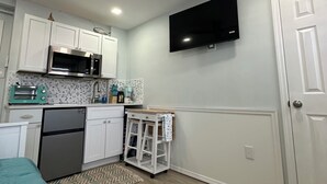 Una cocina compacta con armarios blancos, microondas, tostadora y ventilador de techo.
