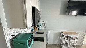 Cocina compacta con armarios blancos, un microondas, un tostador verde y una pequeña mesa de madera.