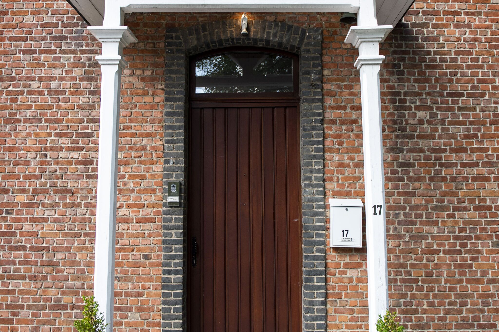 A brick building with a dark brown door, white columns, and a mailbox with the number 17.