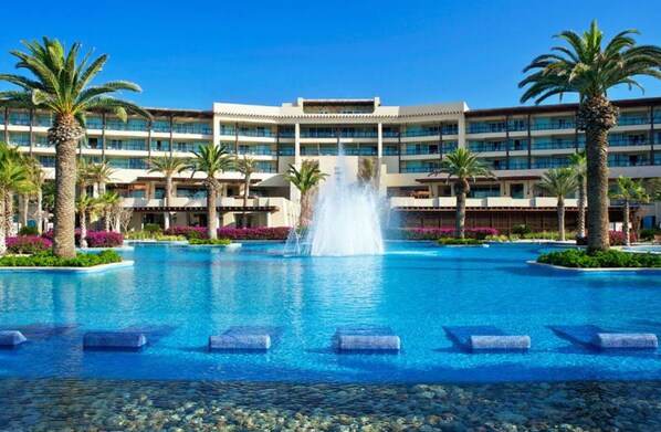 Relax by the pool surrounded by lush greenery and a modern hotel building.
