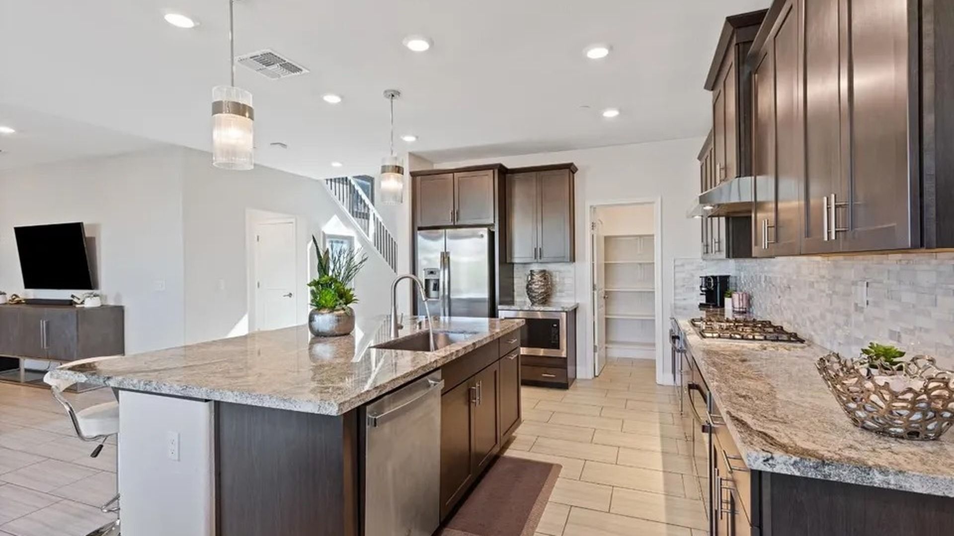 A modern kitchen with a large island, stainless steel appliances, and a staircase leading to another level.