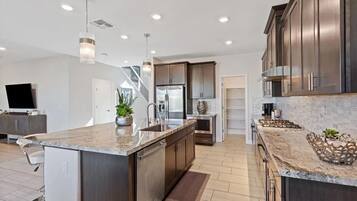 A modern kitchen with a large island, stainless steel appliances, and a staircase leading to another level.