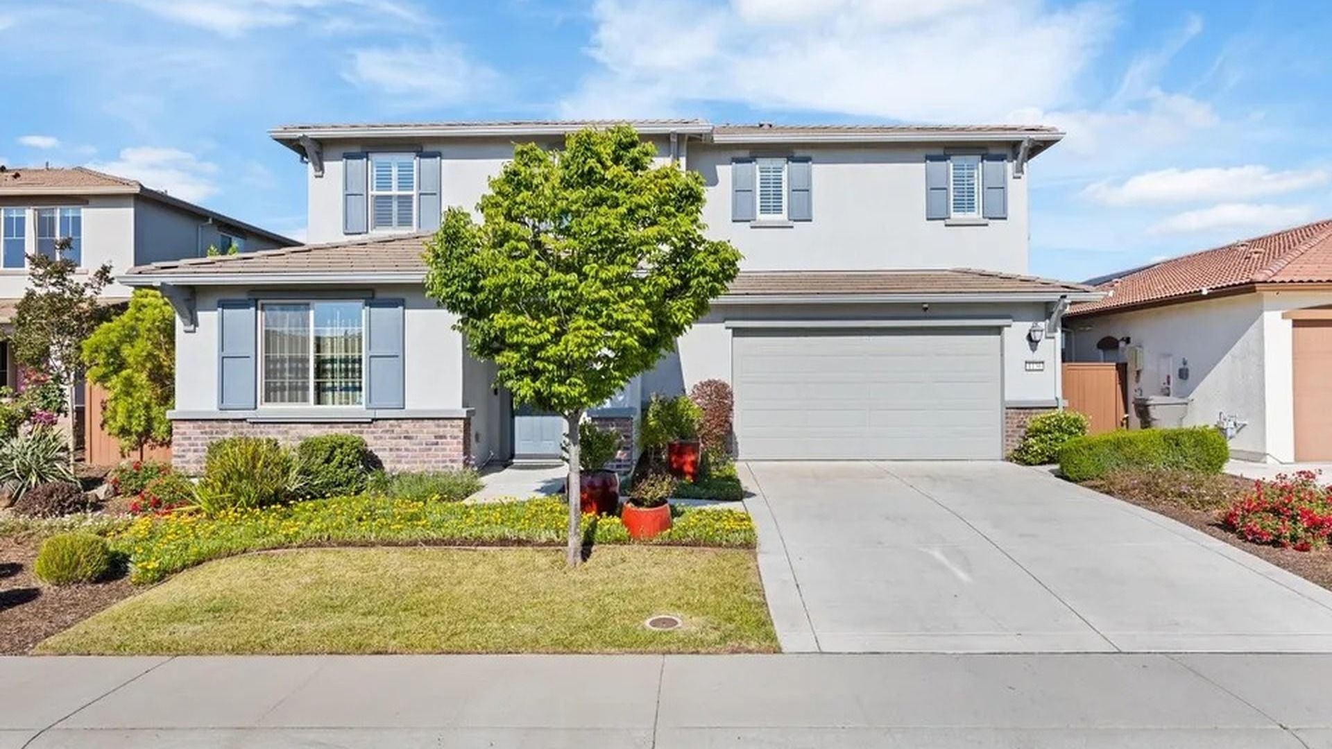A residential house with a garage, a lawn, and a tree in the front yard.