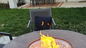 A stone fire pit with a fire burning in the center, surrounded by a circular stone table. - Blue Heaven (Roseville)