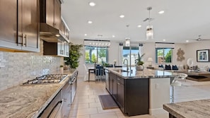 A modern kitchen with a central island, stainless steel appliances, and a dining area with a view. - Blue Heaven (Roseville)