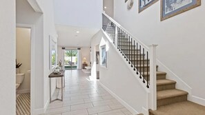 Un pasillo amplio con una escalera que conduce a un piso superior, una puerta a un baño y vistas a un patio.