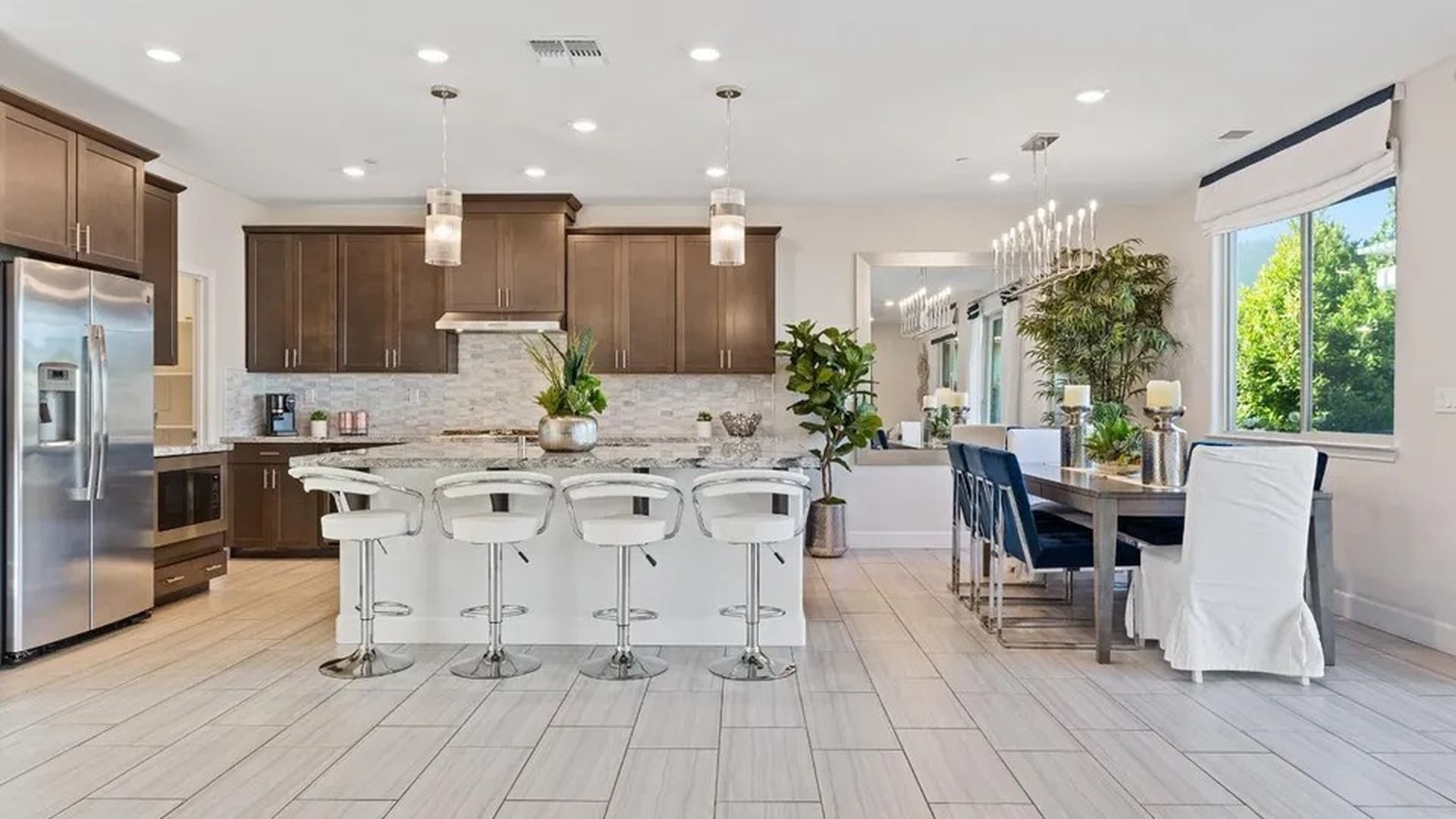 A modern kitchen with a central island, bar stools, and a dining area with a view.