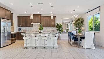 A modern kitchen with a central island, bar stools, and a dining area with a view.