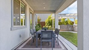 A covered patio with a table and chairs, a doormat, and a view of a backyard with a grill and trees. - Blue Heaven (Roseville)