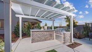 An outdoor patio with a grill and seating area, surrounded by a white pergola and brick accents. - Blue Heaven (Roseville)