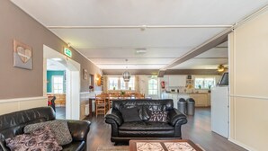 Una sala de estar moderna con un sofá de cuero negro, un cojín estampado y una mesa de centro con una bandeja decorativa. Se ve un comedor con una mesa y sillas de madera al fondo.