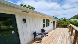 A wooden deck with two chairs and a table, a green door, and a white building with windows. - Family-friendly, playroom w/ air hockey & arcade games, hot tub, mountain views! (Seymour)