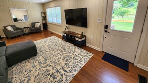 A living room with a ceiling fan, a flat-screen TV, a gray sofa, a coffee table, and a patterned rug. - Family-friendly, playroom w/ air hockey & arcade games, hot tub, mountain views! (Seymour)