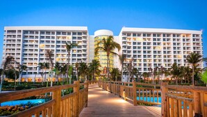 Un hotel con varios edificios altos, un paseo de madera y una zona de piscina.