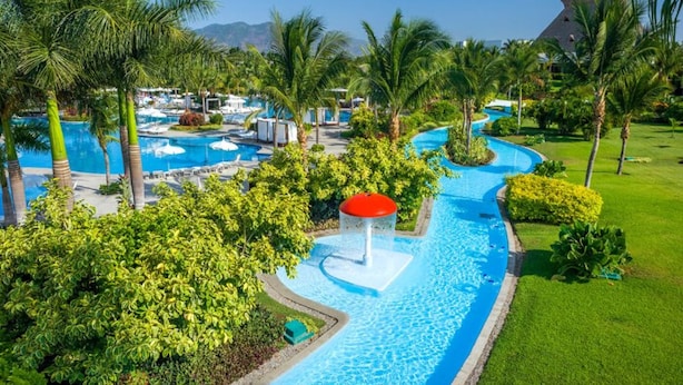 Un resort con varias piscinas, abundante vegetación y un cielo azul despejado.