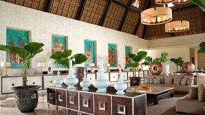 Un hall espacioso con techo alto, grandes macetas y una mesa de centro con jarrones decorativos.