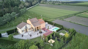 Une grande maison avec une piscine, entourée de champs verdoyants et d’arbres.