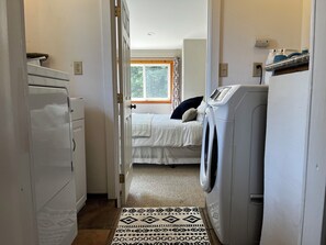 A narrow hallway leading to a bedroom with a bed, a washing machine, and a dryer.
