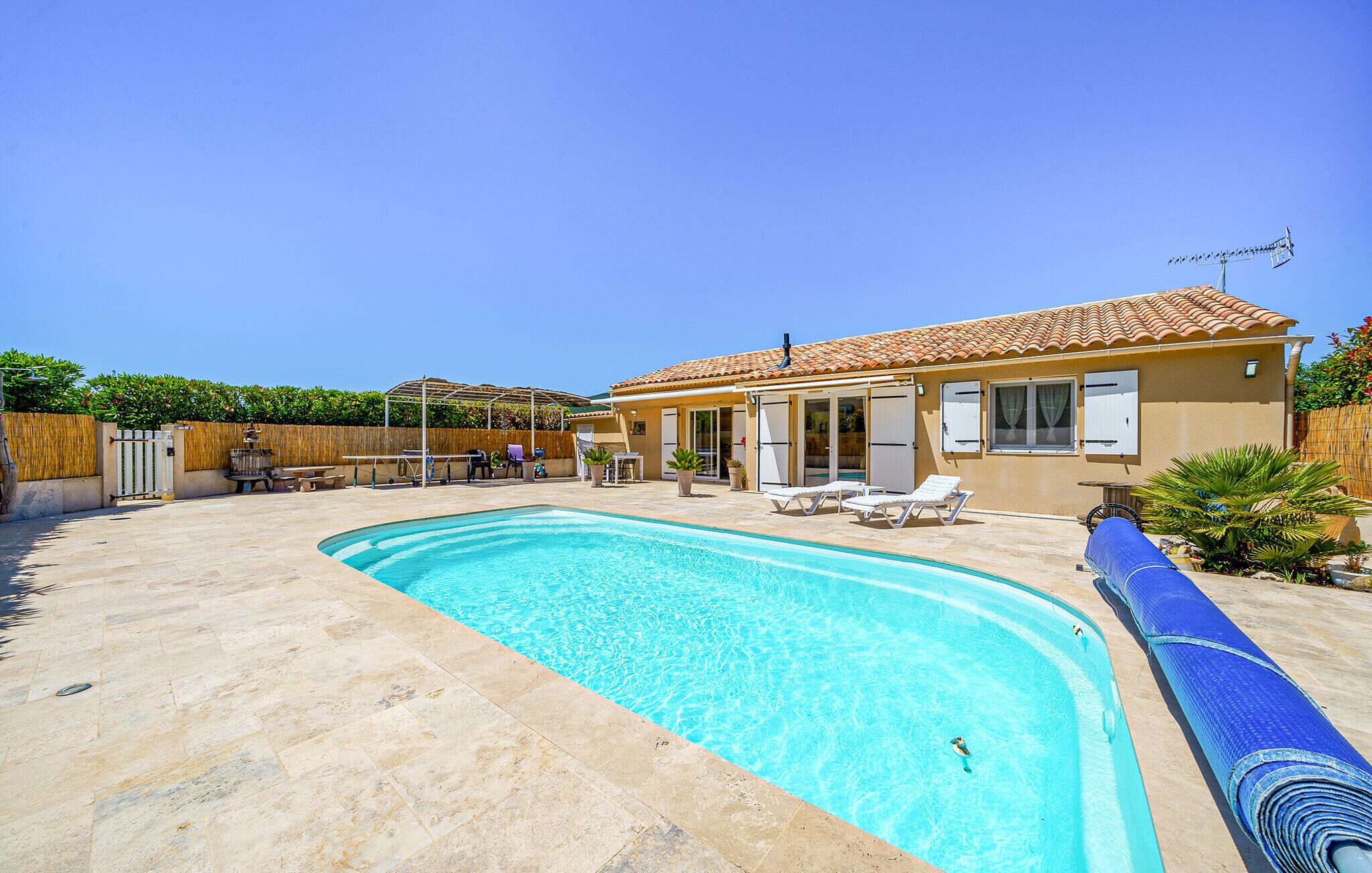 Ein Swimmingpool mit Liegestühlen, eine überdachte Terrasse und ein Haus mit Ziegeldach.