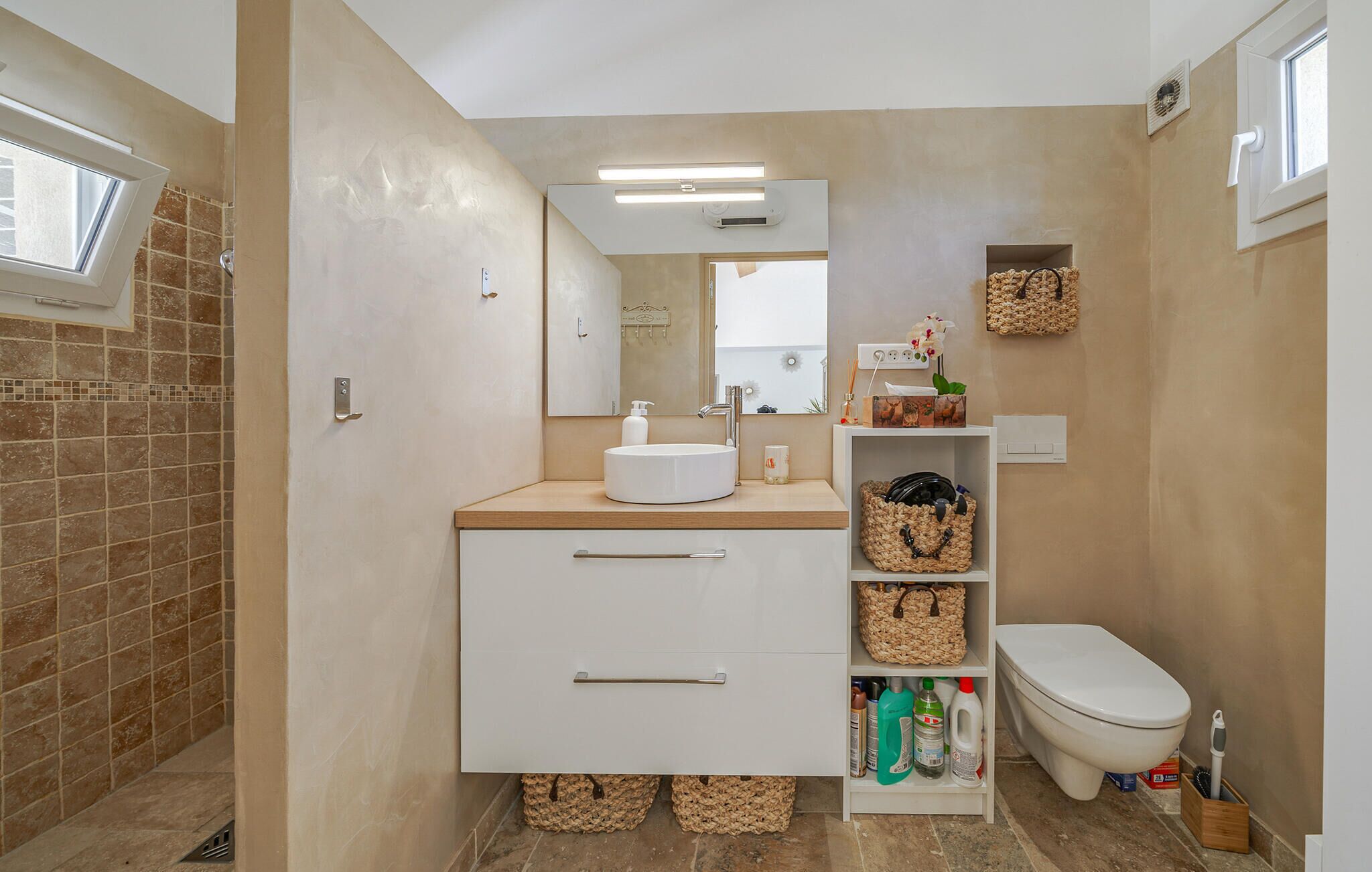 Een moderne badkamer met een wit wastafelmeubel, spiegel, toilet en een douchegedeelte.