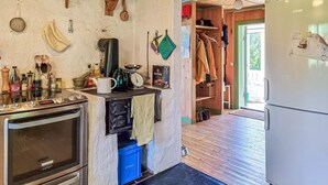 A kitchen with a stove, oven, and various kitchen utensils. There is a refrigerator and a wooden door leading to another room. - 3 bedroom cozy home in Mellerud (Mellerud)