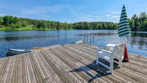 A wooden deck with a rowboat, a white chair, and a striped umbrella. - 3 bedroom cozy home in Mellerud (Mellerud)