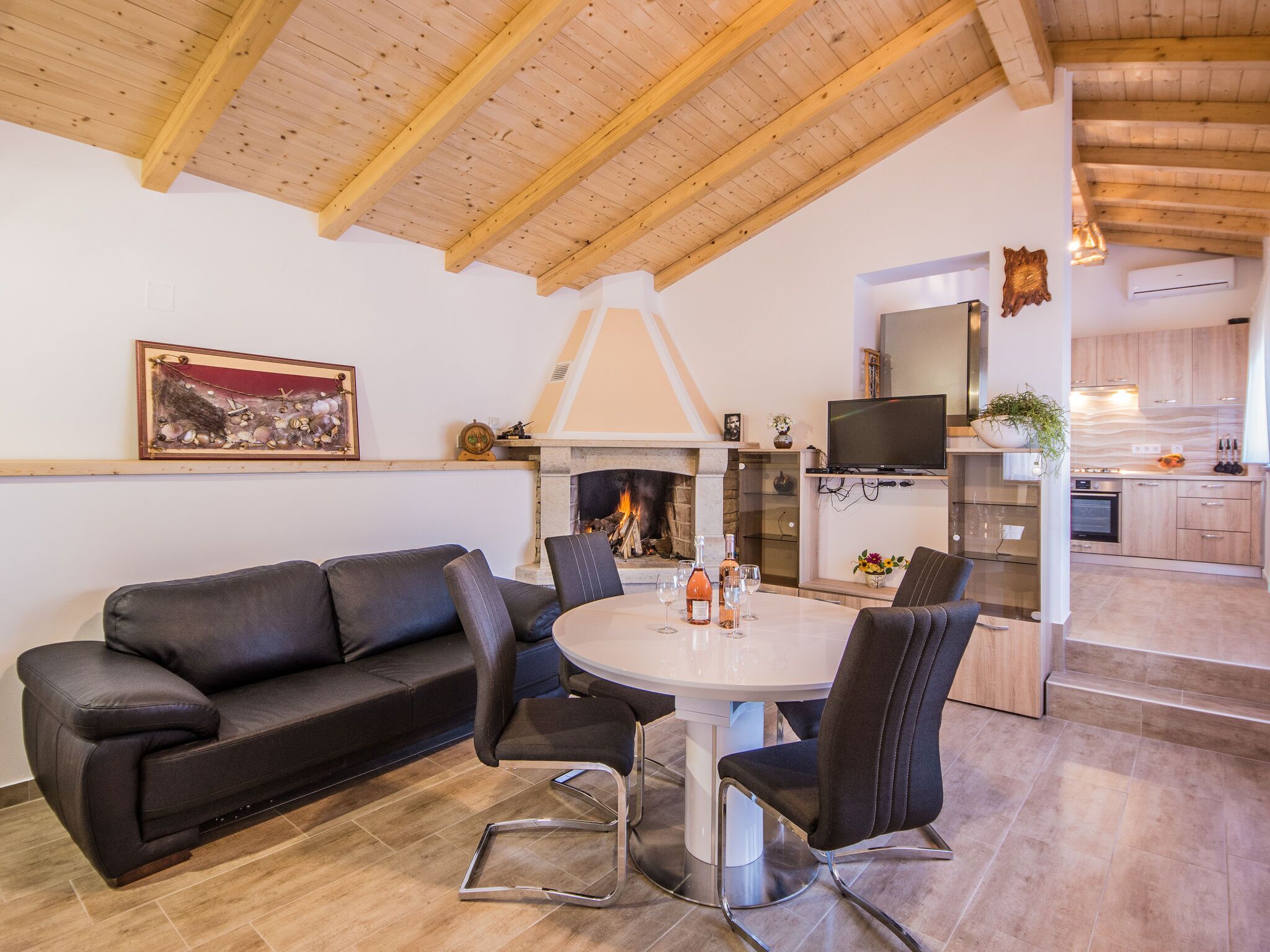 A modern living room with a fireplace, a dining table, and a black leather sofa.