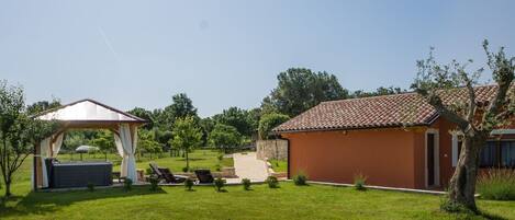 A house with a tiled roof, a covered outdoor seating area, and a lawn.
