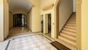 Un vaste hall d’entrée avec un sol à carreaux, un escalier et des portes en arc de cercle.
