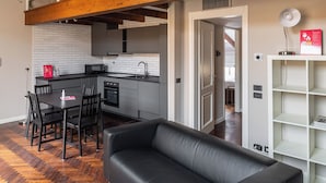 Un salon moderne avec un canapé en cuir noir, un parquet en bois disposé en chevrons et des poutres apparentes en bois au plafond.