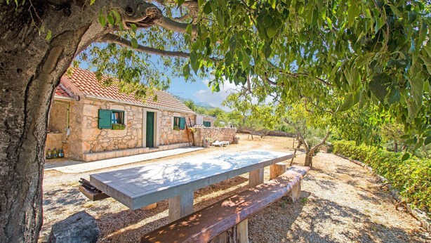 A rustic stone building with a tiled roof, a wooden bench, and a picnic table in a natural setting. - Holiday Home in Seline near the Sea (Seline)