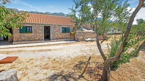 A stone house with a tiled roof, a gravel driveway, and a tree in the foreground. - Holiday Home in Seline near the Sea (Seline)