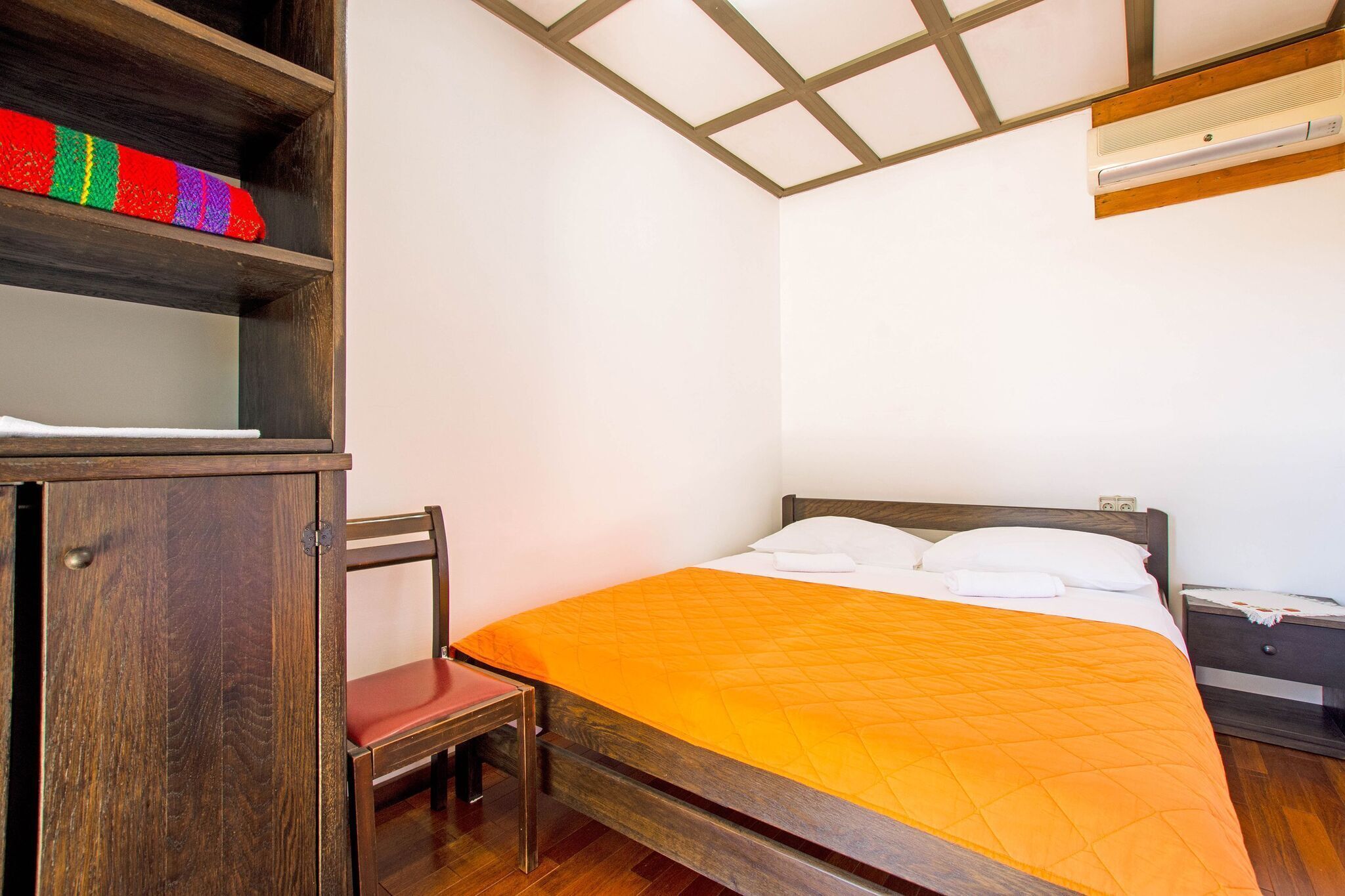 A bedroom with a wooden bed, a small wooden chair, a wooden nightstand, and a shelf with colorful items.