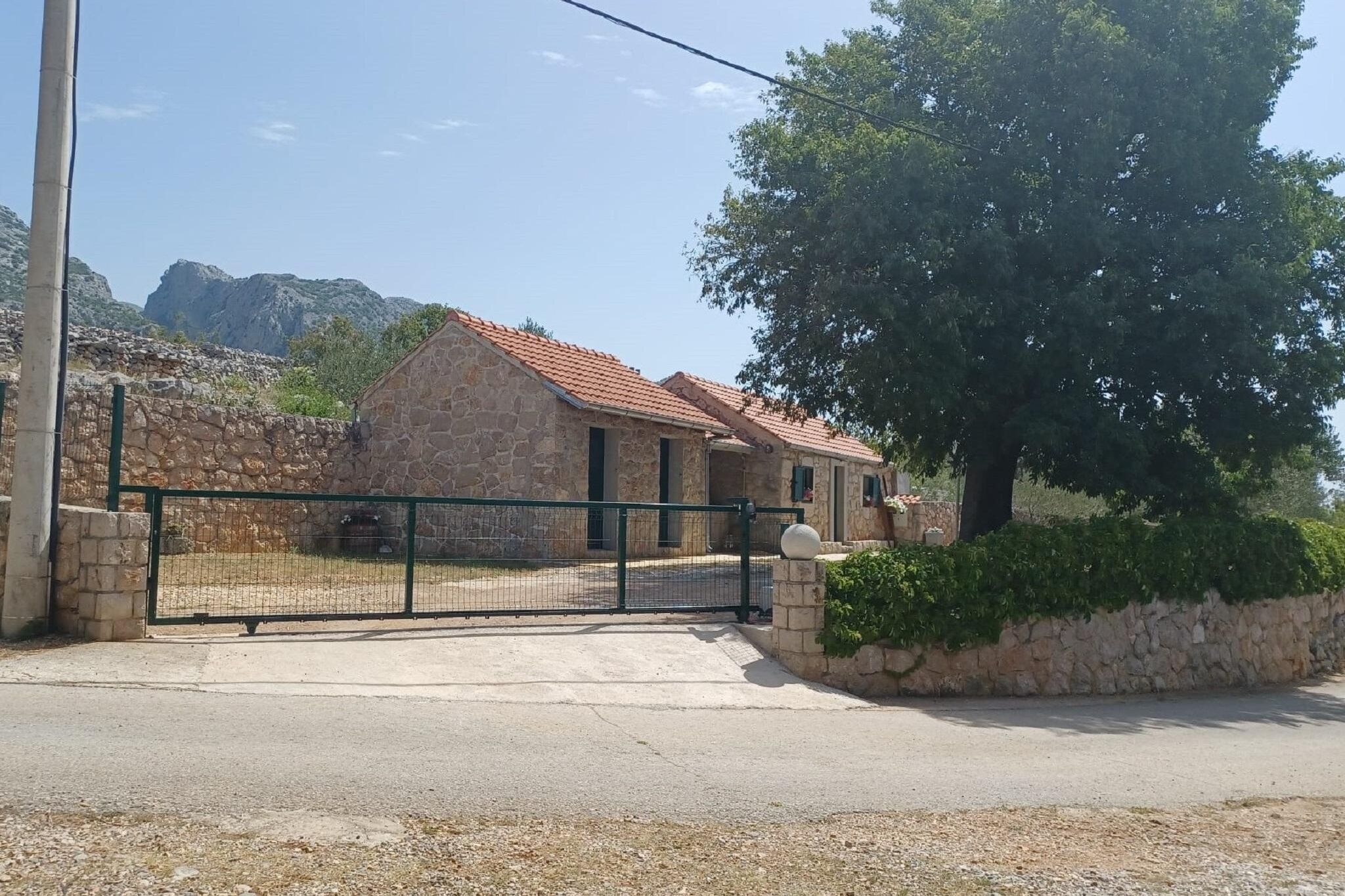 A stone building with a tiled roof, a gated entrance, and a large tree in front.