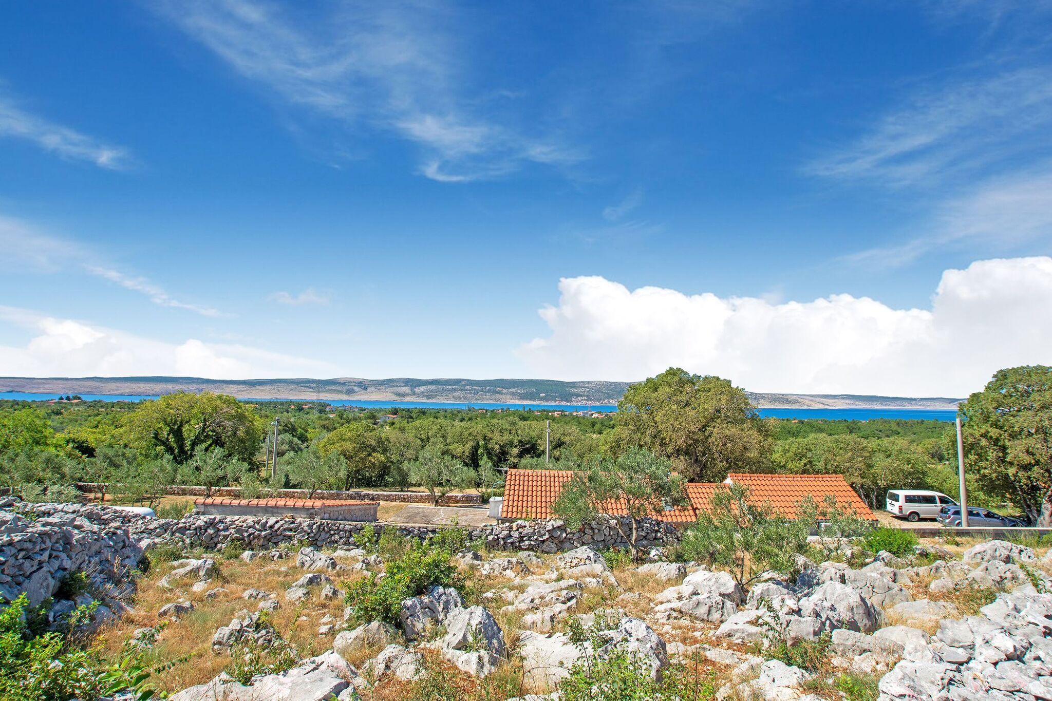 A coastal landscape with a stone wall, trees, and a red-roofed building.