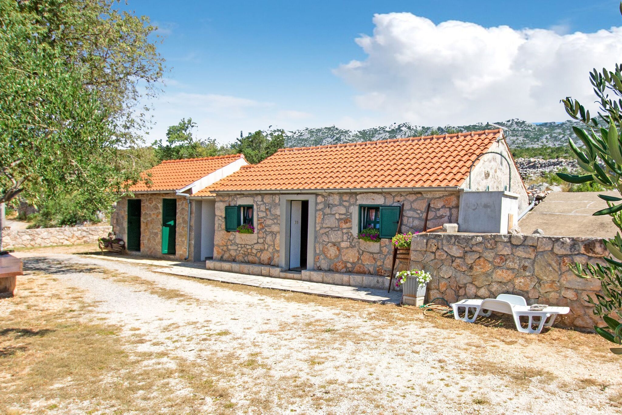 A stone house with a tiled roof, a stone wall, and a gravel driveway.