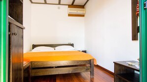 A bedroom with a wooden bed, white pillows, an orange bedspread, a wooden floor, a small wooden nightstand, and a wall-mounted air conditioner. - Holiday Home in Seline near the Sea (Seline)