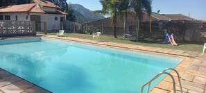 En swimmingpool med ett kaklat poolområde, ett inhägnat område med en pergola och en vattenrutschkana.