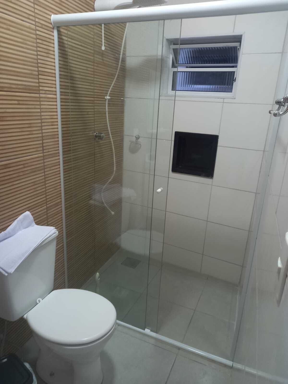 A small, enclosed shower stall with a glass door, a white toilet, and a towel on the floor.