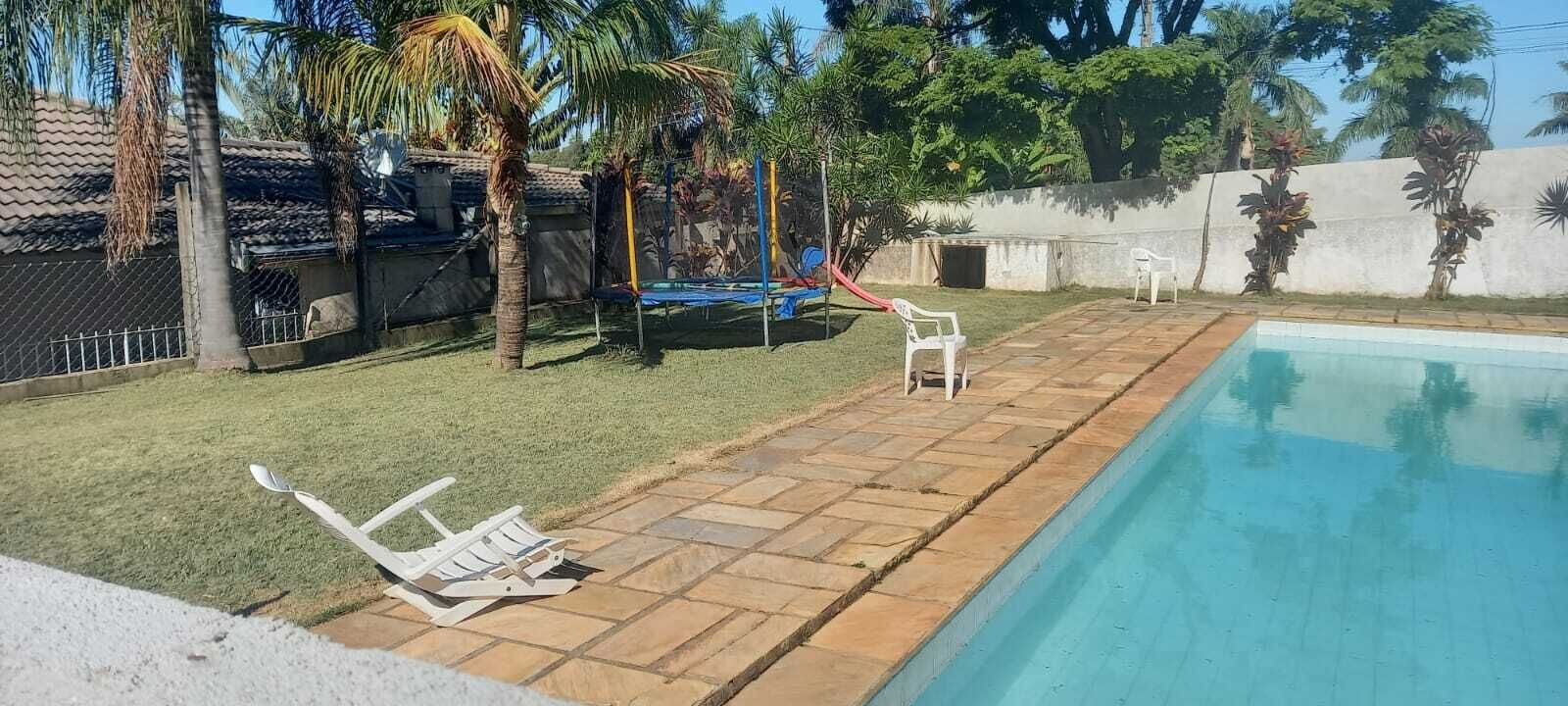 Un patio trasero con piscina, un trampolín y dos sillas de plástico blancas.