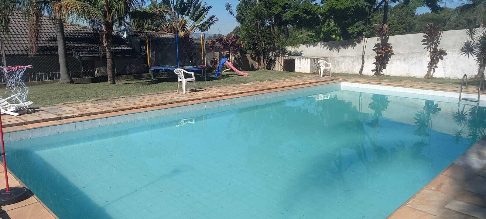A rectangular swimming pool with a tiled edge, surrounded by a tiled deck. There are two white plastic chairs and a small white table near the pool.