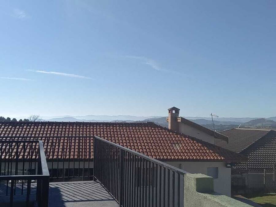 A terrace with a tiled roof, a bell tower, and a view of distant hills.