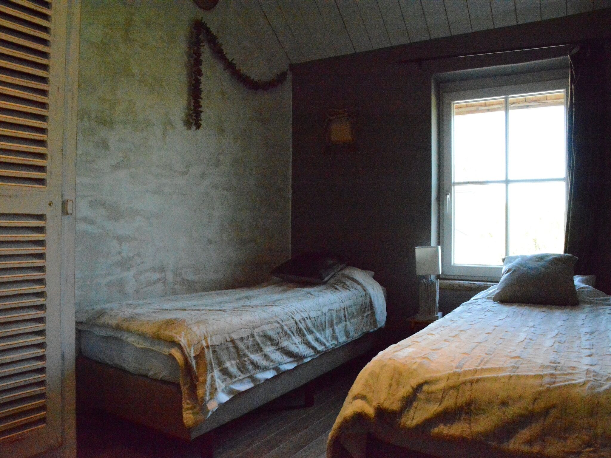 Quarto com duas camas de solteiro, uma janela com luz natural e uma porta com portão.