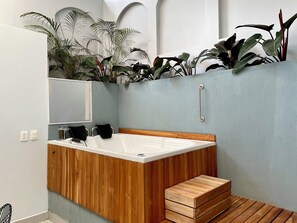 Een moderne badkamer met een houten wastafelmeubel, een witte badkuip en een klein houten krukje.