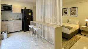 A compact kitchen with a refrigerator, microwave, and sink. There is a small bar area with stools. The room features a bed with a nightstand and a lamp. - Lalinde by Wynwood House (Medellín)