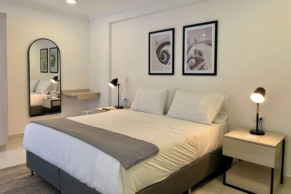 Un dormitorio moderno con una cama, mesitas de noche, un espejo y dos cuadros en la pared.