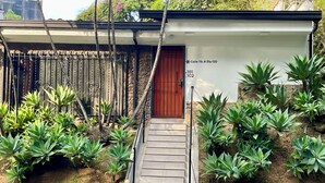 A building with a staircase leading to a wooden door, surrounded by green plants. - Lalinde by Wynwood House (Medellín)